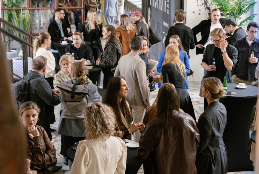 Tłum ludzi rozmawia przy stolikach. W tle widać szarą ściankę z Fashion Forum trends S/S 27.