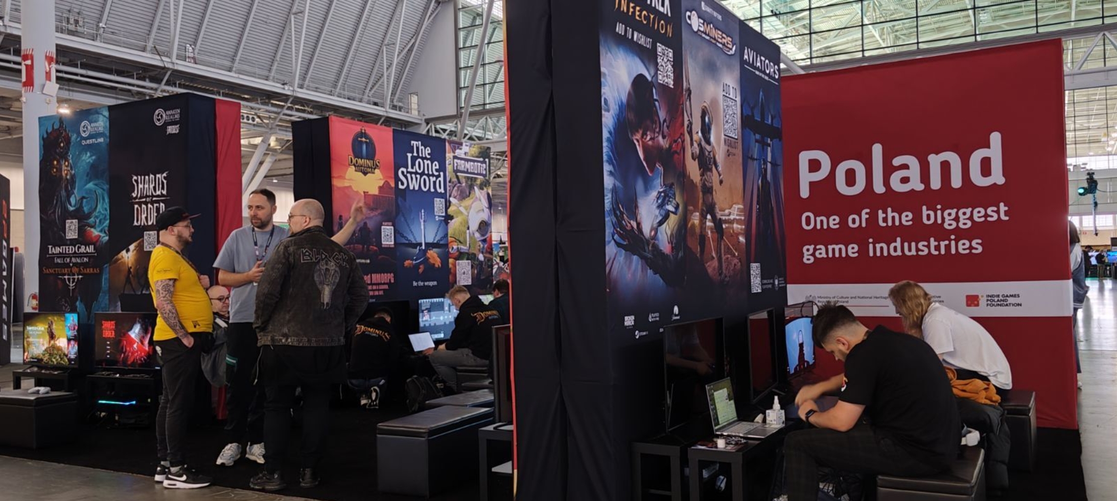 The large, modern exhibition hall houses a promotional stand for Polish game developers. Banners displaying slogans like "Poland One of the Biggest Game Industries," "STAR TREK INFINITY," and "SHARDS OF ORDER" are visible. Visitors chat and play games at monitors.