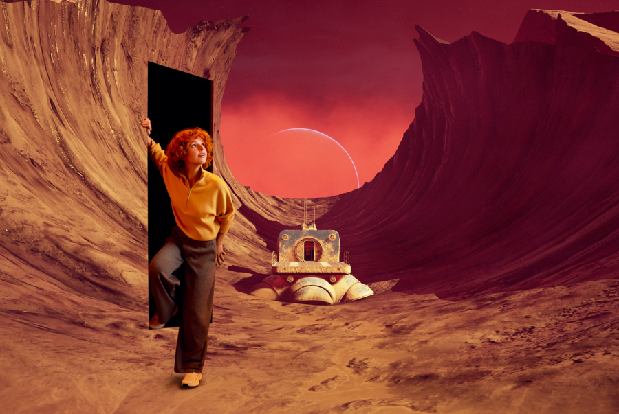 Surrealistyczna scena science fiction – kobieta w żółtym swetrze wyłania się z prostokątnych, ciemnych drzwi w skale na czerwoną, piaszczystą planetę z retro-futurystycznym lądownikiem w kanionie i sierpem planety na niebie.